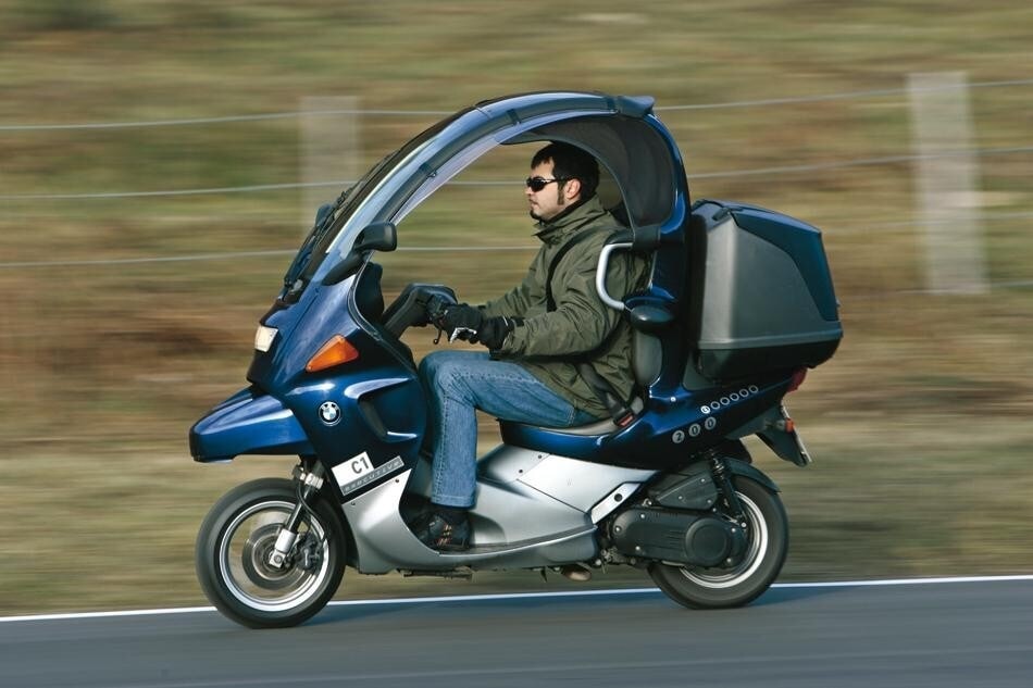 <div class='descrGalleryTitle'>C1</div><div class='descrGalleryText'><p>Altro mezzo di casa BMW con vita brevissima, il C1 arrivò nel pieno del boom degli scooter, guarda caso con una formula anticonvenzionale. <b>Anticonvenzionale a dir poco, perché aveva il tetto rigido e si guidava senza casco </b>grazie a una speciale omologazione.&nbsp;Cercava di far propri i <b style="font-size: 0.8125rem; background-color: transparent;">vantaggi degli spostamenti in auto</b>, anche se la protezione dalla pioggia non era un granché. Sul C1 la seduta è a metà tra quella di una moto e quella di un’auto, <b>il sedile è provvisto di cinture di sicurezza </b>e sopra la testa del conducente sta un rollbar integrato in quello che di fatto è un tetto. <b>Il passeggero, invece, sta fuori dalla cella e deve mettersi il casco...</b> La formula era fortemente divisiva: c'è chi lo usa (sempre senza casco) ancora oggi e chi lo detesta. <b>Nel complesso vendette poco </b>e nonostante la lunga gestazione (il primo prototipo risale al 1992) dopo essere entrato in produzione nel 1999 rimase in commercio solo sino al 2003.</p>
</div>